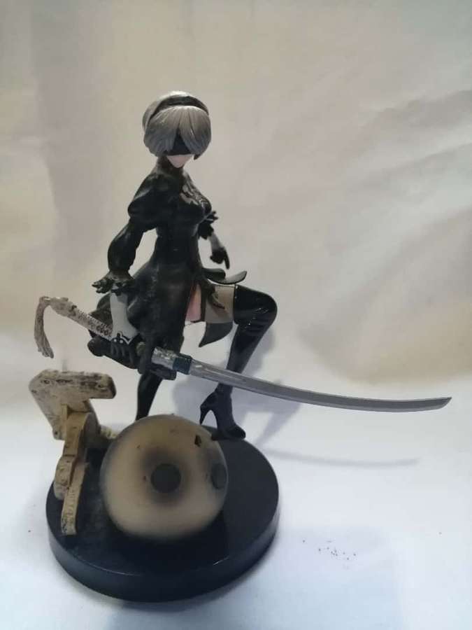 Anime-Figur einer weiblichen Kriegerin mit silbernem Haar, die ein Katana auf einem schwarzen Sockel mit Schädel und Holz hält. — 2b Bilder