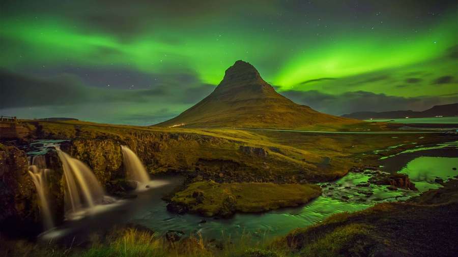 Green northern lights illuminate a mountain and waterfall at night. — 4K Aurora Wallpaper