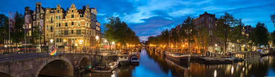 Amsterdam canal at twilight with historic buildings and boats lit by warm lights. — 4K Ultra Widescreen Wallpaper