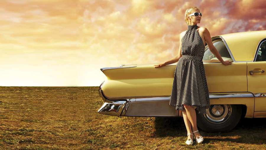 Woman in polka dot dress leaning on vintage yellow car at sunset. — 50s Style Wallpaper
