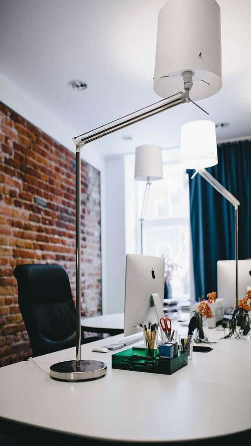 Minimalist modern office desk with lamp and computer against brick wall. — 720p Office Background