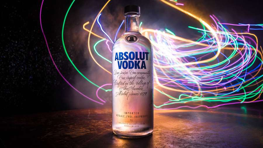 A clear vodka bottle with neon light trails swirling behind it in a dark setting. — Absolut Wallpaper