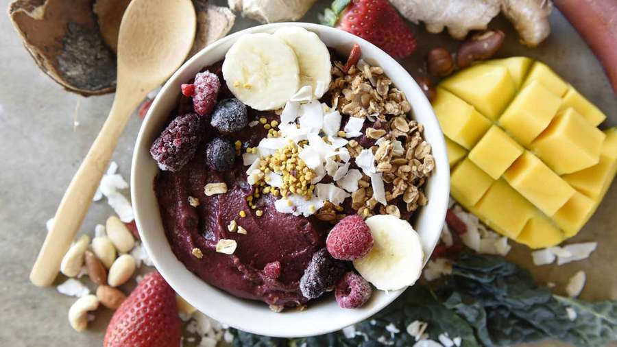 A colorful smoothie bowl with fruit nuts and granola on a wooden tray. — Acai Wallpaper