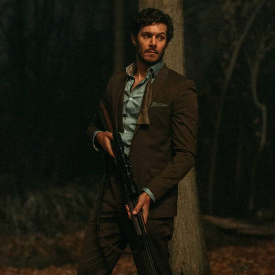 Mann in braunem Anzug hält Gewehr in dunklem Wald bei Nacht — Adam Brody Hintergrundbild