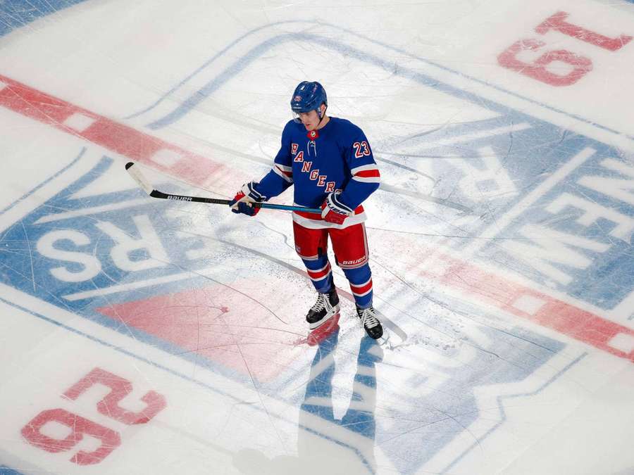 Hockey player in Rangers uniform on ice rink holding stick. — Adam Fox Wallpaper