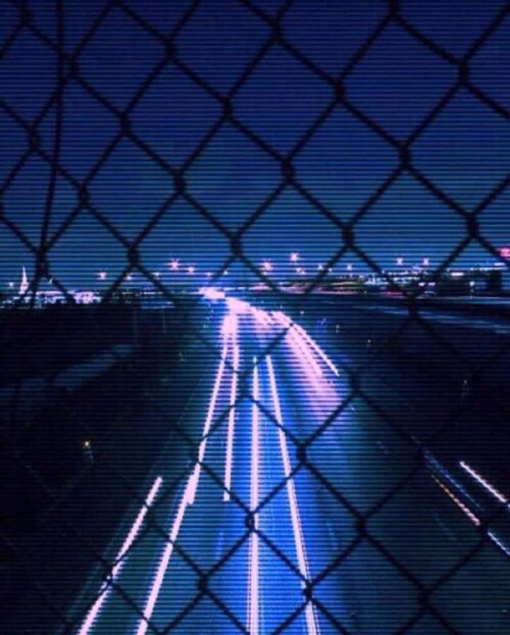 Night highway with blue light trails seen through a chain-link fence. — Aesthetic Blue Grunge Wallpaper