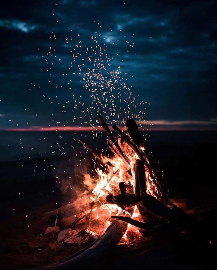 Campfire sparks flying at twilight over water — Aesthetic Fire Wallpaper