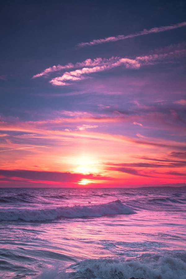 Vibrant pink and orange sunset over the ocean with waves crashing. — Aesthetic Sunset Background