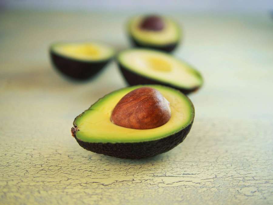 Cuatro aguacates partidos por la mitad con huesos sobre una superficie amarilla agrietada. — Aguacate Fondos de pantalla