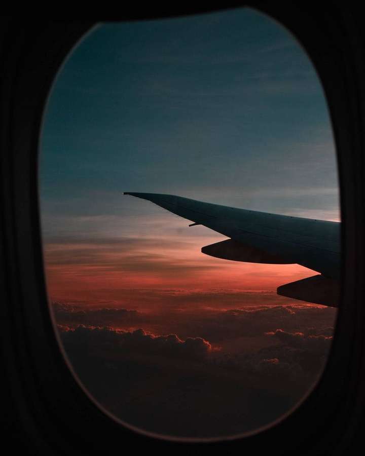 Airplane wing silhouetted against a vibrant sunset sky seen through a window. — Airplane Window Wallpaper