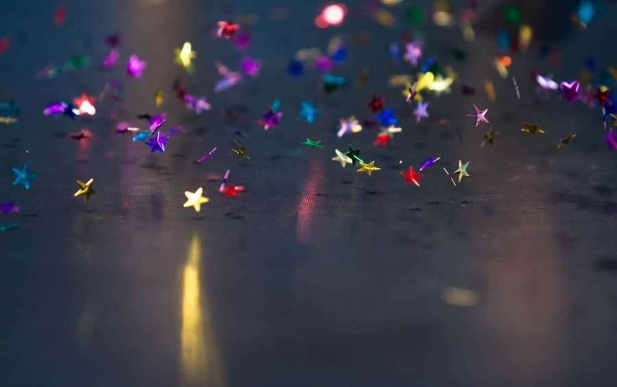 Confeti colorido en forma de estrella esparcido sobre una superficie oscura reflectante con luz cálida. — Alegre Fondos de pantalla