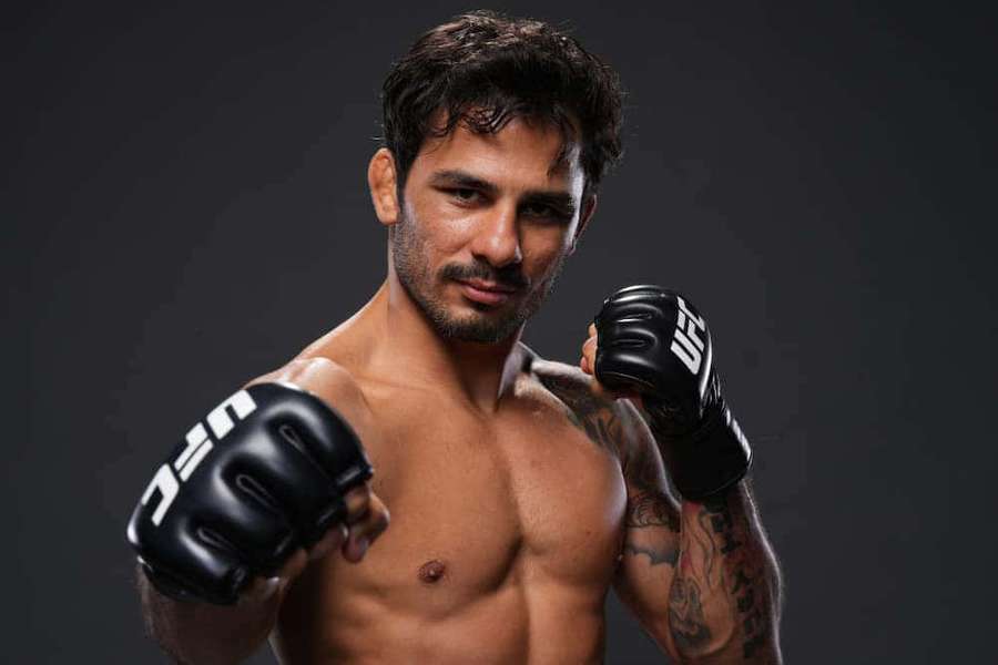 A shirtless male fighter with tattoos wearing black UFC gloves in a studio. — Alexandre Pantoja Wallpaper
