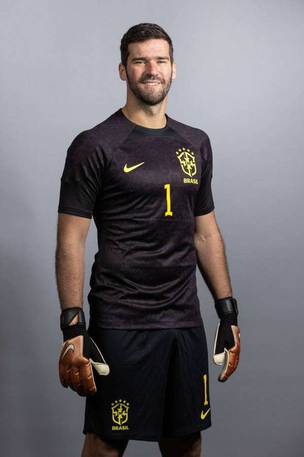 Brasilianischer Fußballtorwart in schwarz-gelber Uniform, der Handschuhe hält — Alisson Becker Bilder