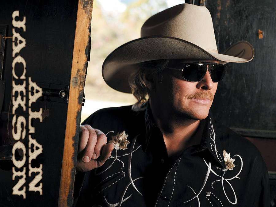 Alan Jackson mit Cowboyhut und Sonnenbrille, an ein Schild gelehnt. — Allan Jackson Wallpaper