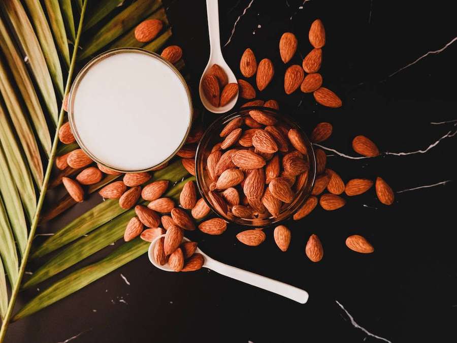 Almond milk and whole almonds on a black marble surface with palm leaves. — Almond Wallpaper
