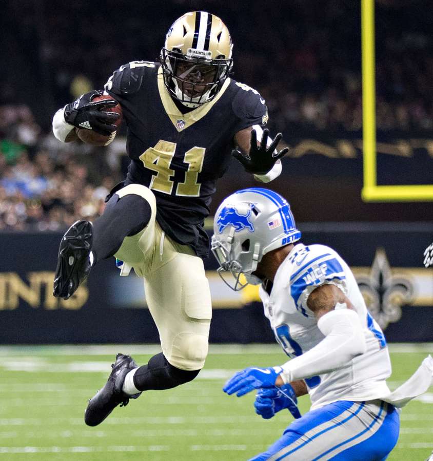 Football player leaps with ball as defender dives for tackle during night game. — Alvin Kamara Background