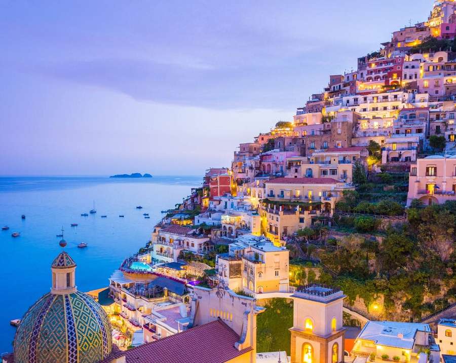 Coastal cliffside village glowing at twilight with sea and boats in background. — Amalfi Coast Wallpaper