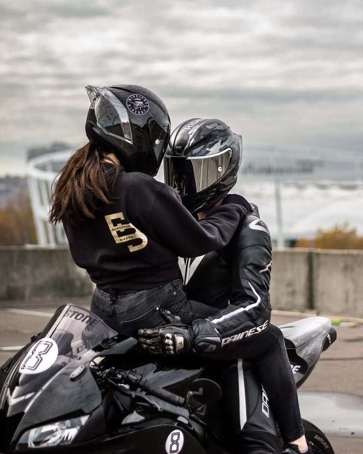 Dos pilotos con cascos se abrazan en una moto negra en un día nublado. — Amantes Fondos de pantalla