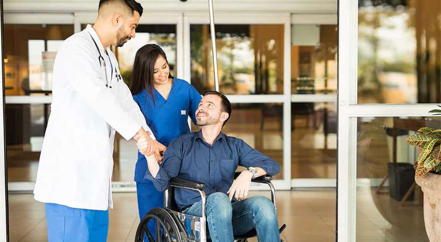 Doctor and nurse assisting a smiling man in a wheelchair indoors. — Ambulatory Wallpaper