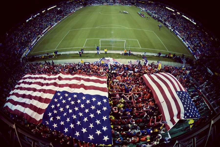 Crowd of soccer fans holding giant American flags in a stadium at night. — American Background