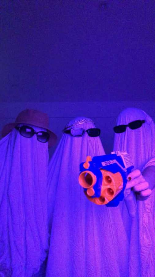 Tres personas disfrazadas de fantasma con gafas de sol sosteniendo una pistola Nerf bajo luz púrpura. — Amistad Fondos de pantalla