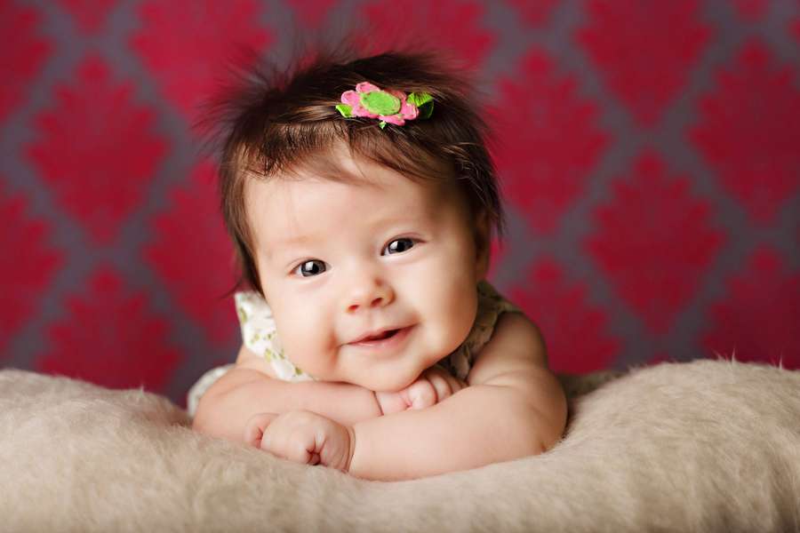 Um bebê feliz usando uma tiara floral rosa descansa sobre uma superfície bege fofa. — Amor de bebê Papéis de Parede