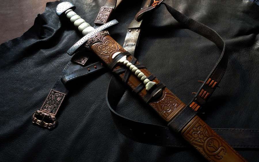 A decorative fantasy sword with bone handle and leather scabbard on dark leather. — Ancient Weapons Wallpaper