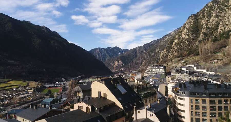 Mountain village with buildings nestled in a valley under a blue sky with clouds. — Andorra Wallpaper