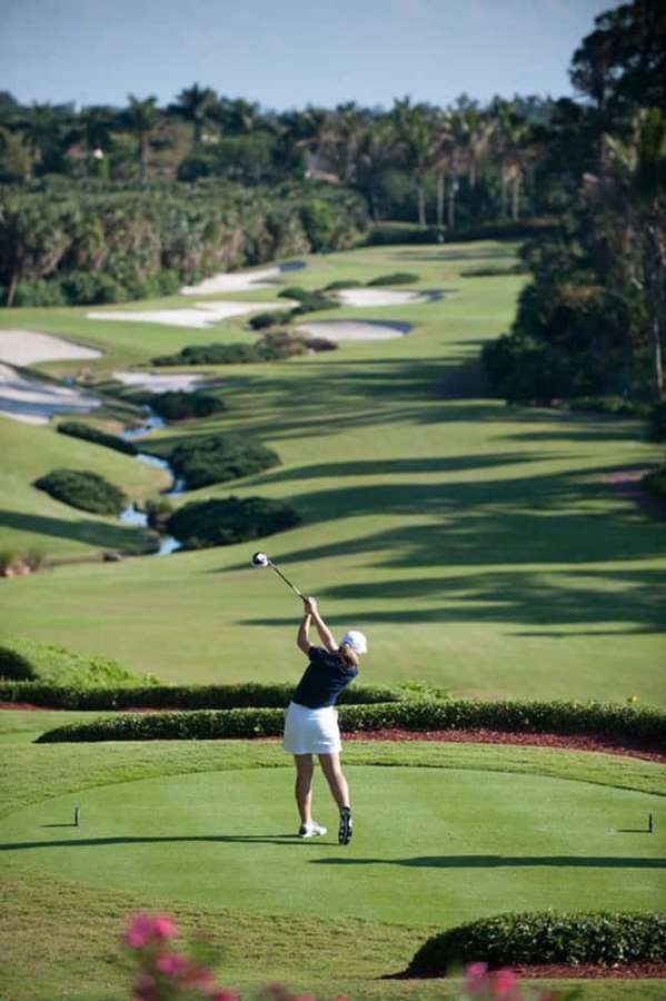 Woman swinging golf club on sunny tropical golf course with palm trees and water hazards. — Android Golf Course Background