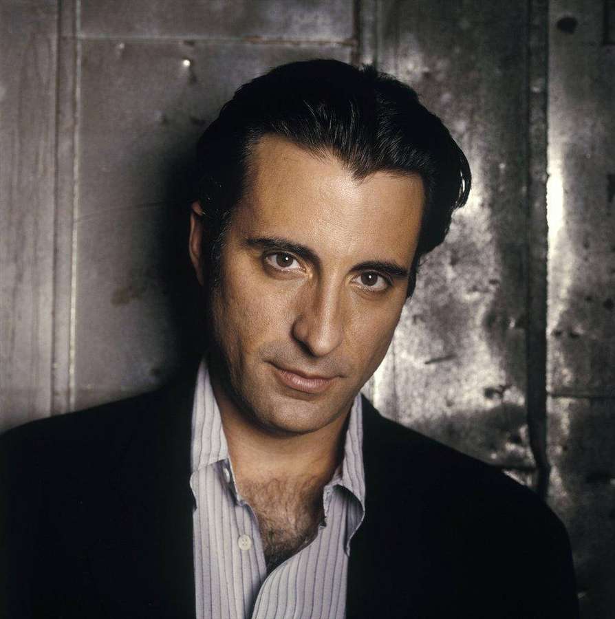 A man in a suit leans against a metal wall with intense eyes. — Andy Garcia Background