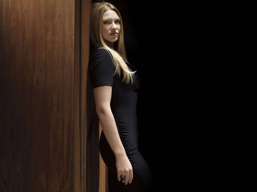 A woman in a black dress leans against a wooden door in a dark studio setting. — Anna torv Wallpaper