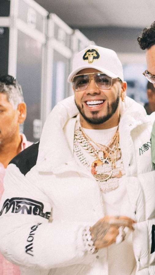 Mann in weißer Moncler-Jacke und Goldketten lächelt drinnen. — Anuel Bilder