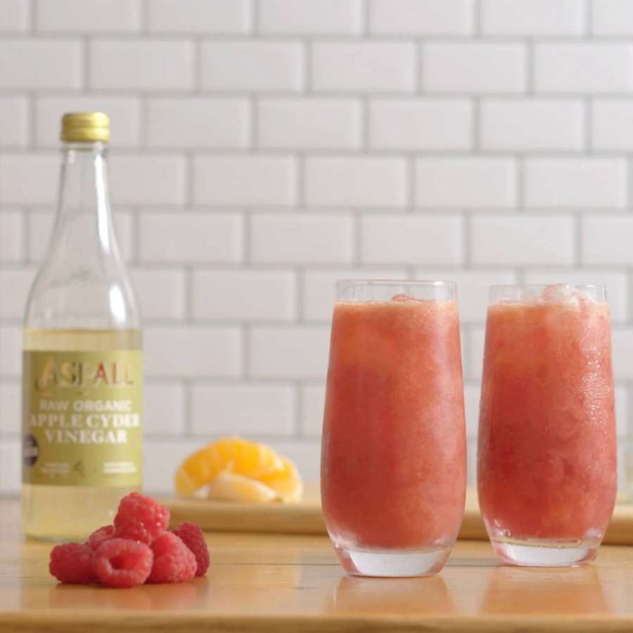 Zwei Gläser Himbeergetränk mit Eis neben Apfelessigflasche und frischen Himbeeren. — Apfelessig Wallpaper