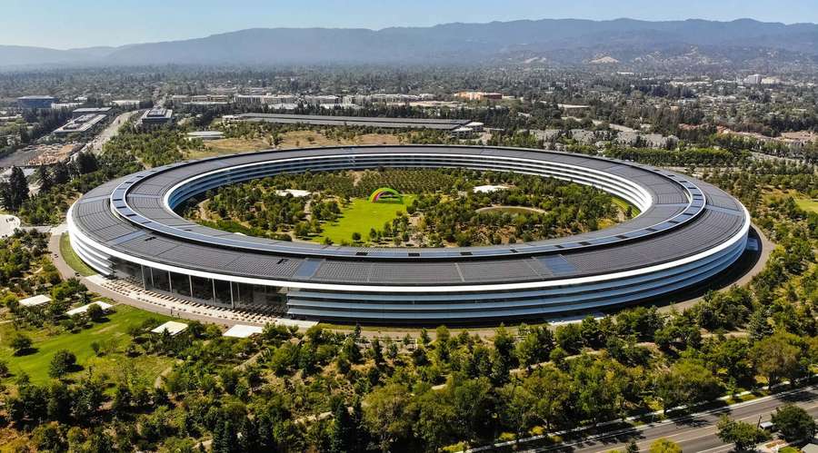 Apple Park's futuristic circular building surrounded by trees and mountains on a sunny day. — Apple Park Wallpaper