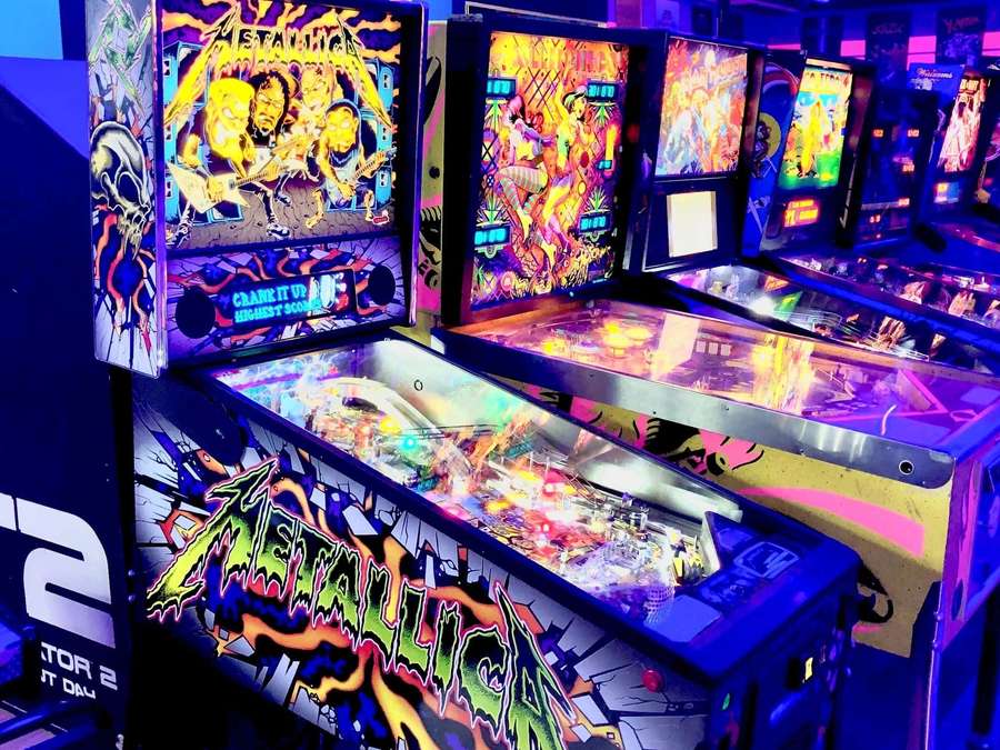 Neon-lit pinball machines with Metallica artwork in a retro arcade. — Arcade Games Wallpaper