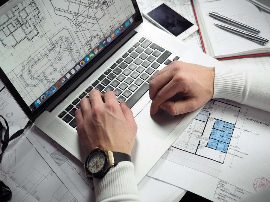 Pessoa trabalhando em laptop com plantas arquitetônicas na mesa — Arquiteto Papéis de Parede