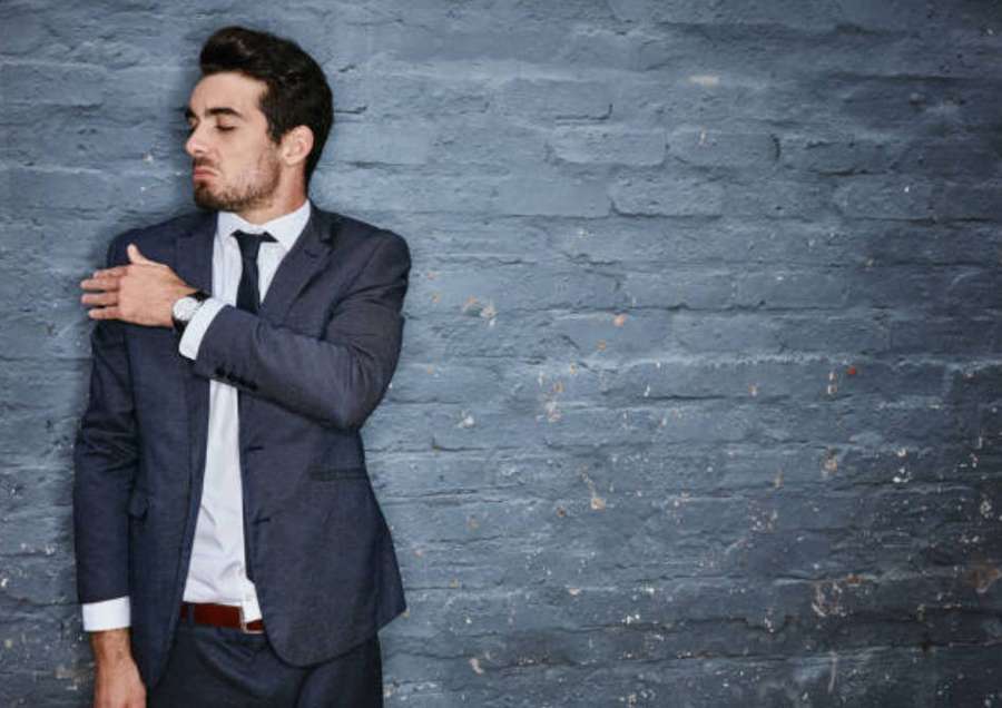 Man in suit checking watch against gray brick wall — Arrogant Wallpaper