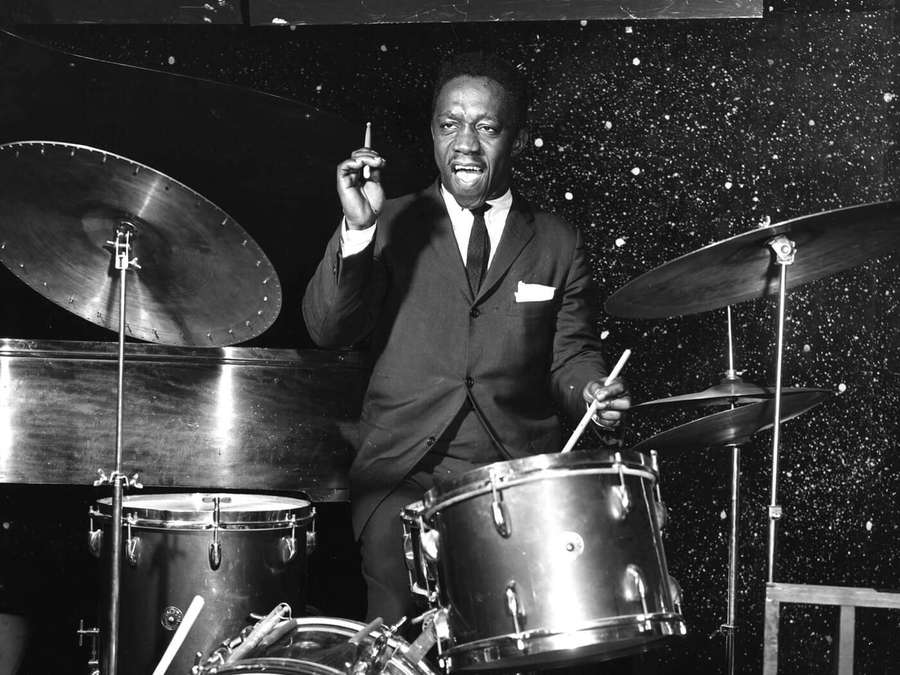 Jazz drummer in suit holding cigarette behind drum set under starry lights. — Art Blakey Wallpaper