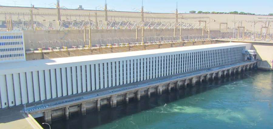 Large hydroelectric dam releasing water into a river at sunset. — Aswan High Dam Wallpaper