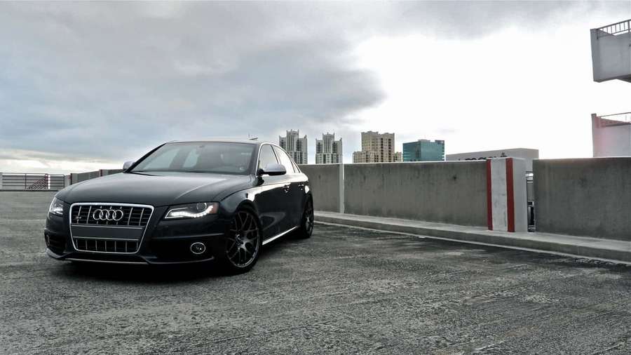 Zwarte Audi sedan geparkeerd op een parkeergarage op het dak met stadsgezicht op de achtergrond. — Audi A4 Achtergronden