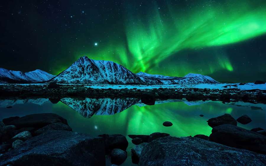Aurora boreal verde ilumina montañas nevadas y su reflejo en un lago helado y tranquilo por la noche. — Aurora boreal Fondos de pantalla