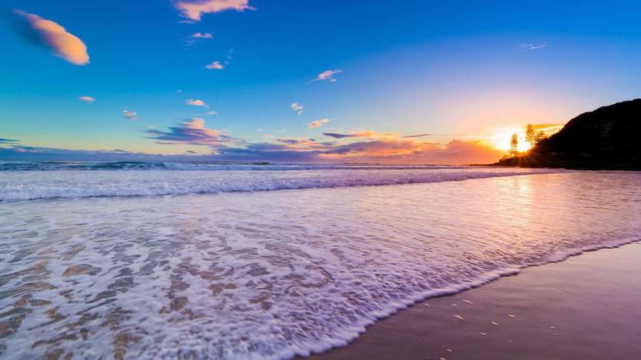 Sunset over ocean with waves washing onto sandy beach — Australia Beach Wallpaper