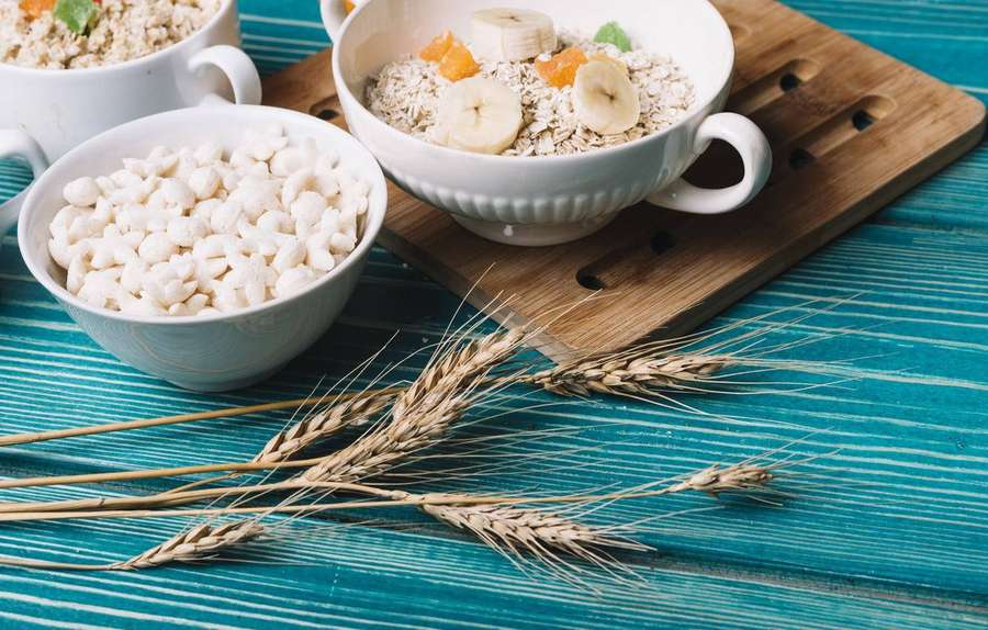 Três tigelas de cereais e aveia com banana e frutas secas em uma mesa de madeira azul-petróleo com talos de trigo. — Aveia Papéis de Parede