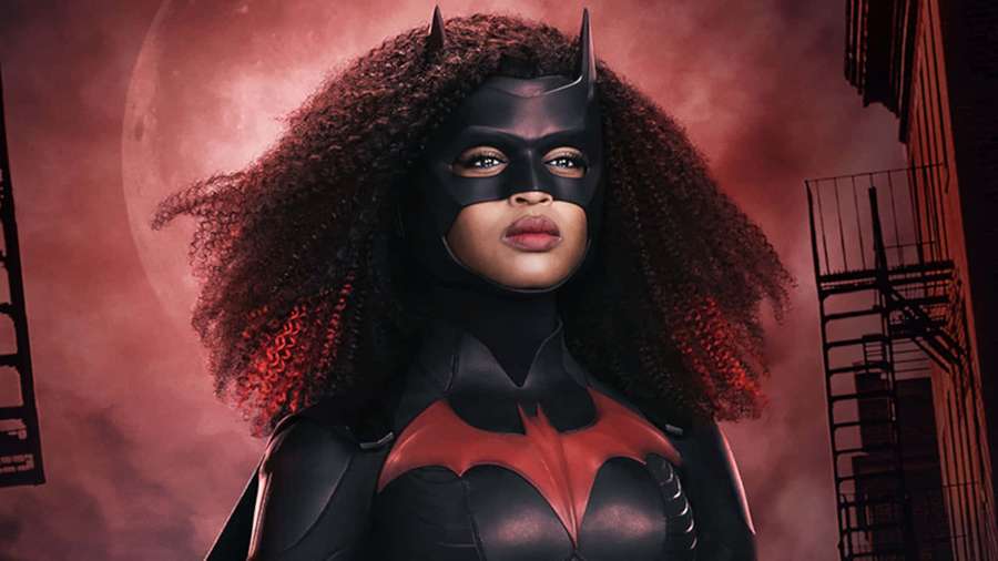Batwoman in black and red suit with curly hair against a red moon and city buildings. — Awesome Batman Background