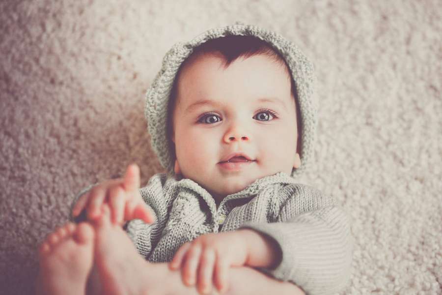 Ein Baby mit grauer Strickmütze und -outfit liegt auf einem beigen Teppich. — Baby Junge Wallpaper