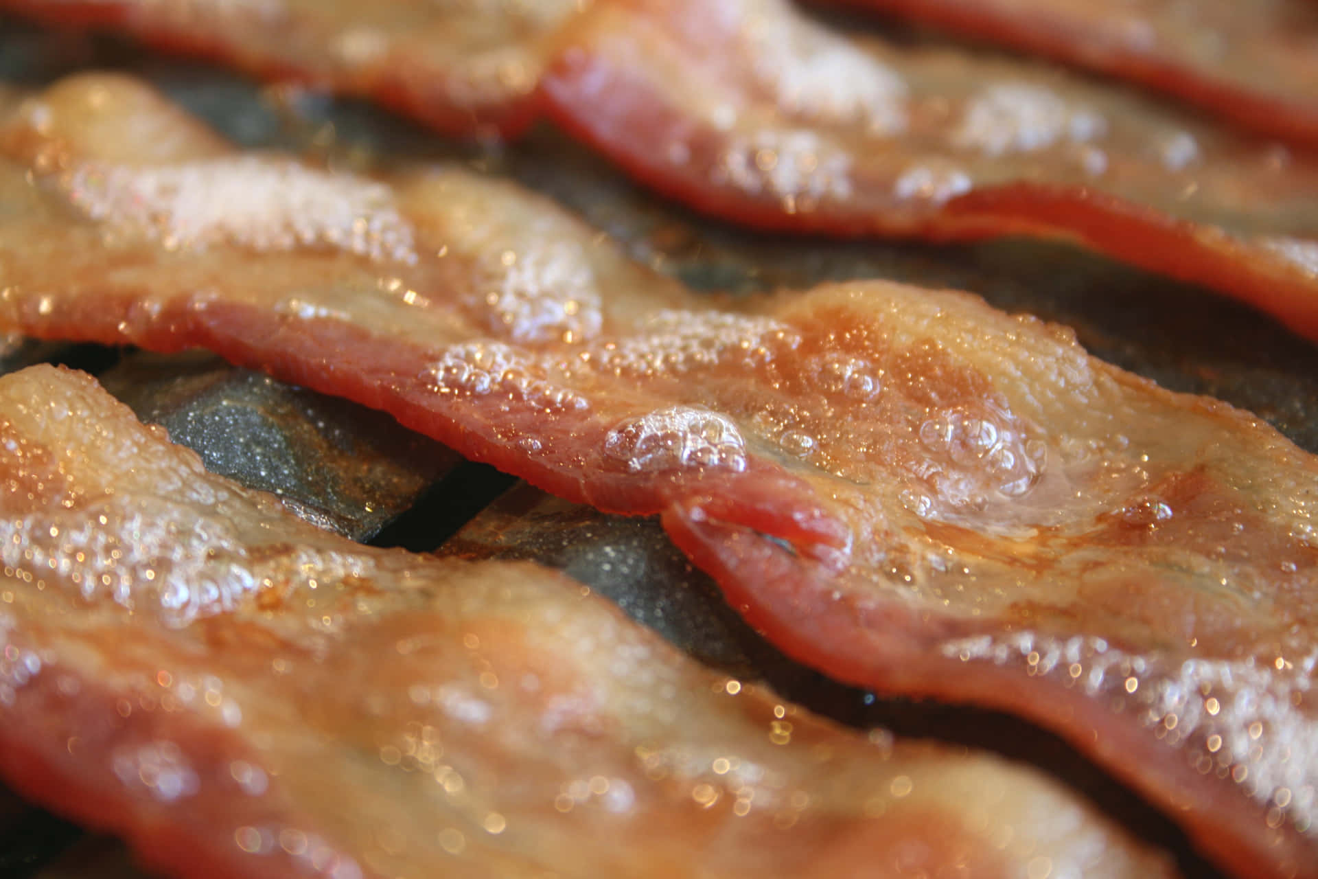 Krispiga baconremsor som fräser på en mörk stekhäll med bubblande fett. — Bacon Bakgrundsbilder