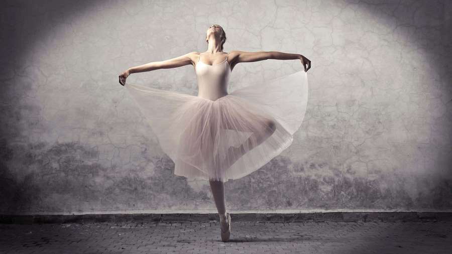Ballerina in white tutu dancing en pointe under spotlight against cracked wall. — Ballet Background