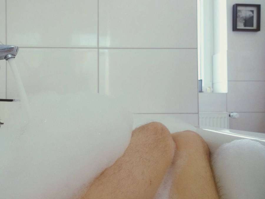 Persona sumergida en una bañera espumosa con agua corriendo del grifo. — Bañera Fondos de pantalla