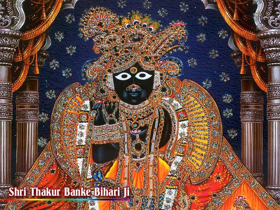 Black deity with white eyes adorned in gold jewelry and orange robes in a temple setting. — Banke Bihari Wallpaper