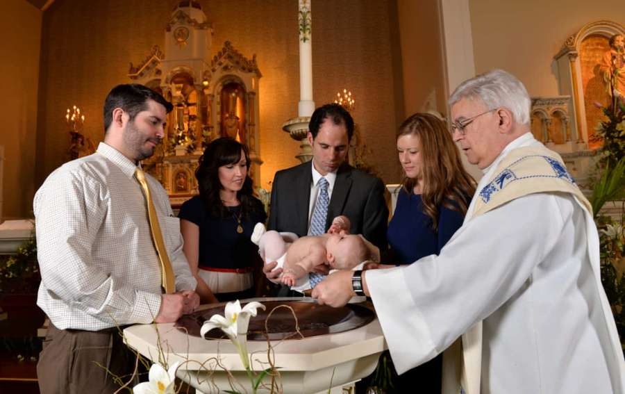 A priest baptizes a baby during a church ceremony with family present. — Baptism Picture
